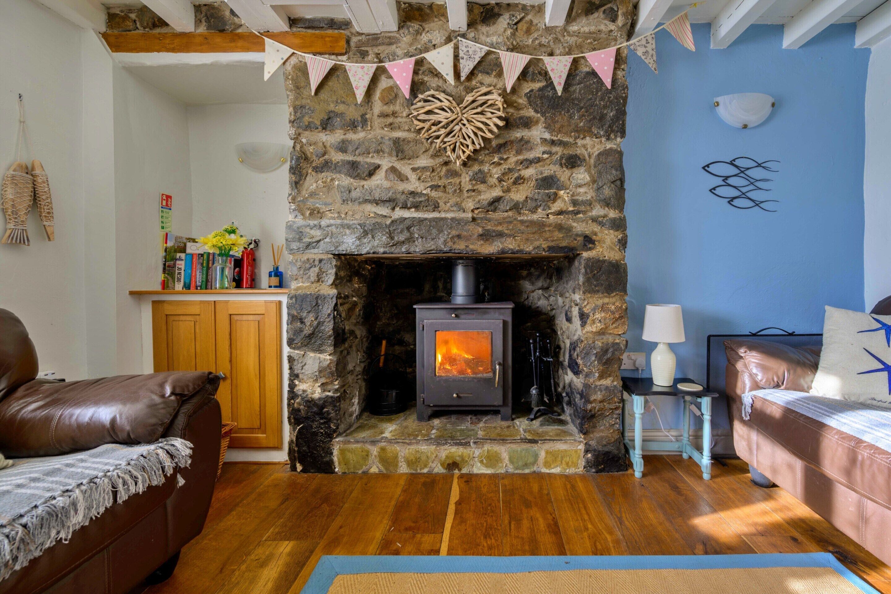 A cozy living room with a stone fireplace, wooden flooring, and a blue accent wall.
