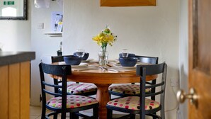 Ein Essbereich mit einem runden Holztisch, vier Stühlen mit gepunkteten Kissen, einer Vase mit gelben Blumen und blauen Schüsseln.