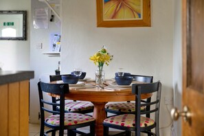 A dining area with a round wooden table, four chairs with polka-dotted cushions, a vase with yellow flowers, and blue bowls. - Beachfront Llyn Peninsula Cottage for 6 (Pwllheli)