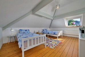 A bedroom with a sloped ceiling, a window with a view of greenery, a bed with a blue ocean-themed bedspread, a small table with a lamp, and a colorful rug. - Chic Country Club Lodge With Hot Tub (Harlech)