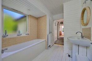 Ein Badezimmer mit einer Badewanne, einem Waschbecken, einem Fenster mit Segelbooten und einer Meerfarn-Dekoration.
