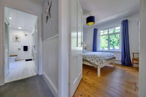 Ein Schlafzimmer mit Bett, einem Vorhangfenster, Holzboden und einer Tür zu einem weiteren Raum.