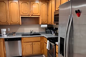 A kitchen with wooden cabinets, a stainless steel refrigerator, a dishwasher, and a coffee maker. - Saratoga Comfort: 
A Peaceful Private Stay (Aiken)