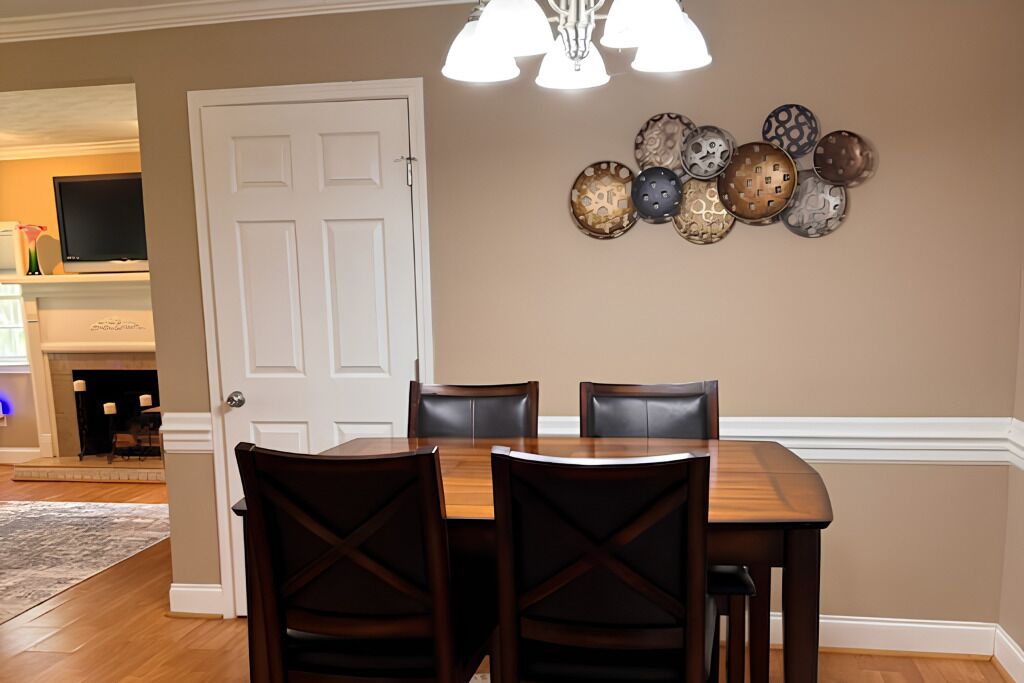 A dining area with a wooden table and four chairs, a white door, and a wall-mounted decorative plate arrangement.