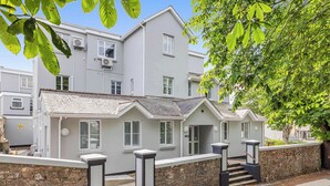 A two-story building with a grey facade, multiple windows, and a stone wall at the base. - The Maycliffe - Compact Studio Close to Beach (Torquay)