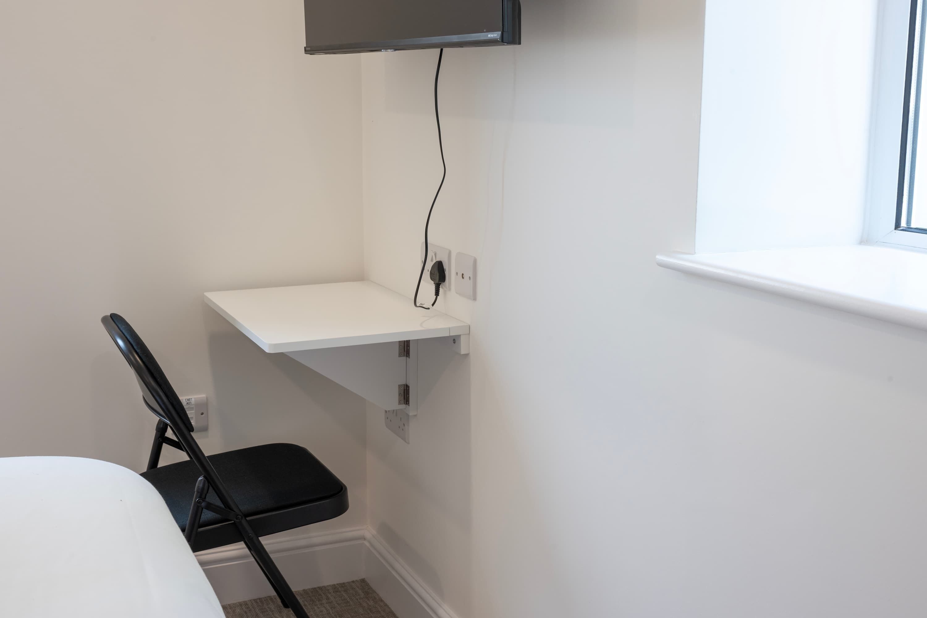A corner of a room with a white desk, a black chair, and a wall-mounted TV.