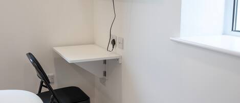 A corner of a room with a white desk, a black chair, and a wall-mounted TV.