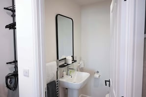 A bathroom with a white sink, a mirror, a towel rack, and a hairdryer on a shelf.