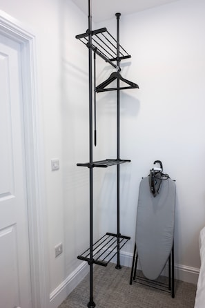 A black metal drying rack with multiple shelves in a room with white walls and a grey floor.
