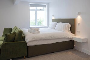 A bedroom with a bed, a green armchair, a bedside table, and a window. - The Maycliffe - Bright Contemporary Studio (Torquay)