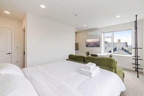 Une chambre d’hôtel avec un grand lit, un canapé vert, un bureau et une fenêtre donnant sur la ville.