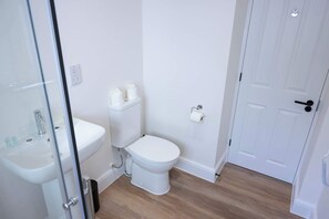 Une petite salle de bain propre, équipée de toilettes, d’un lavabo et d’une douche à parois en verre.