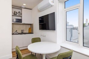 Eine kleine Küche mit einem weißen Tisch und Stühlen, einer eingebauten Mikrowelle und einem Fenster mit Blick auf Gebäude.