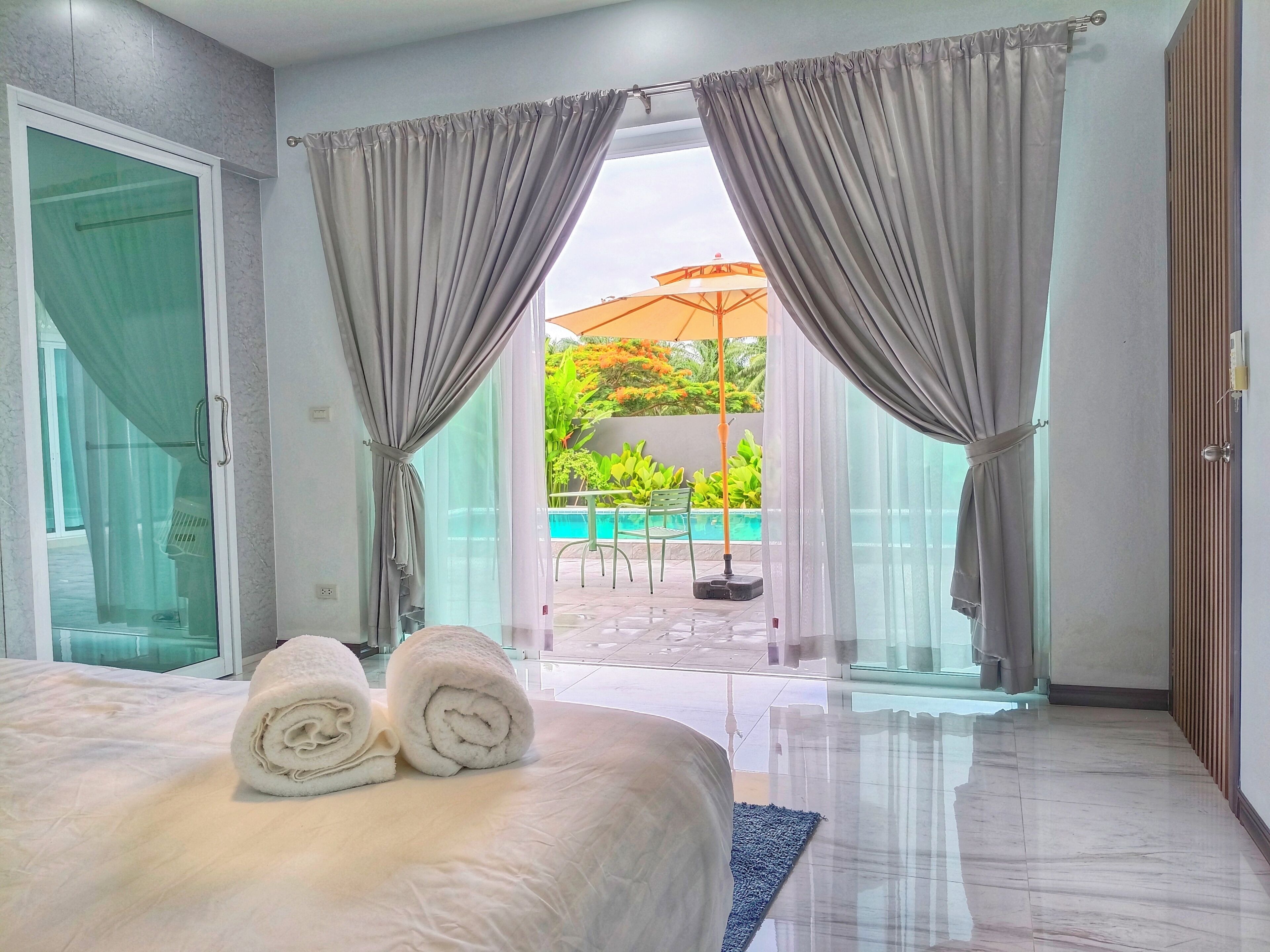A hotel room with a bed, two rolled towels, a glass door, and a view of an outdoor pool area.