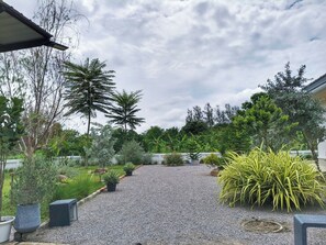 Uma trilha de cascalho serpenteia por um jardim com diversas plantas e árvores.
