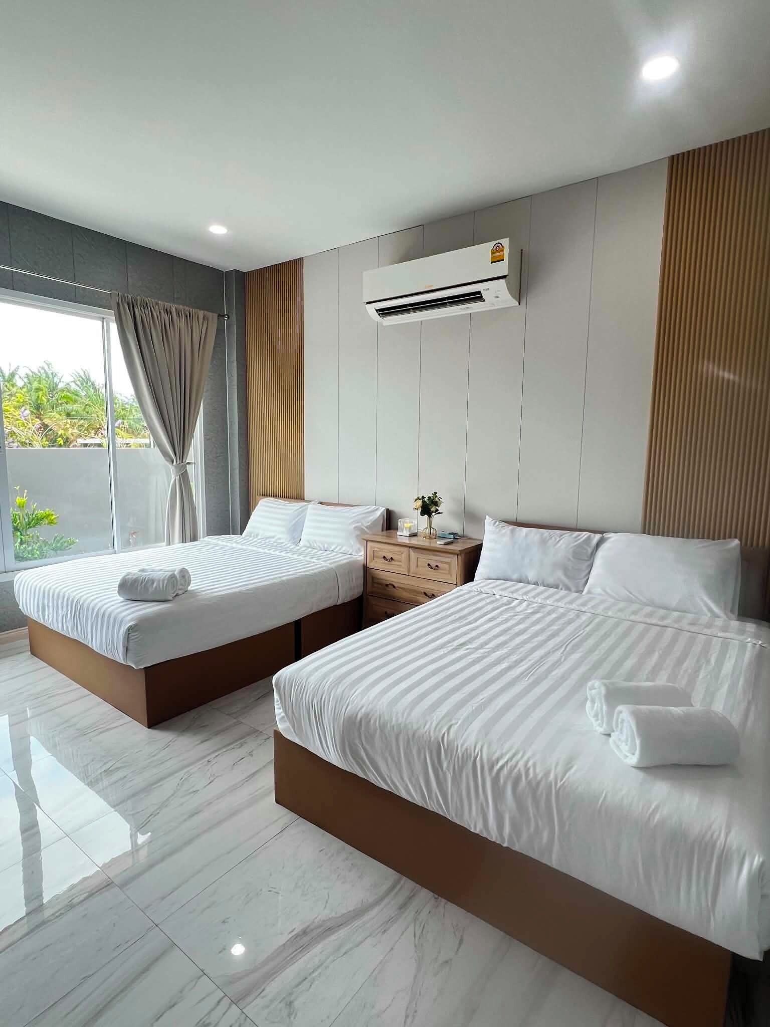Ein Hotelzimmer mit zwei Betten, einem Nachttisch, einer Klimaanlage und Blick auf Grünfläche.