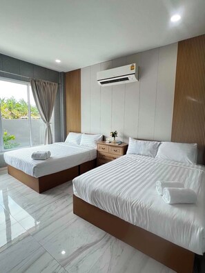 A hotel room with two beds, a nightstand, an air conditioning unit, and a view of greenery outside.
