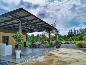 Uma área externa coberta com piso de concreto, plantas em vasos e um espaço para sentar.