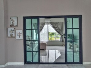 A room with a large sliding glass door leading to an outdoor area, a sofa, a small table, and framed pictures on the wall.