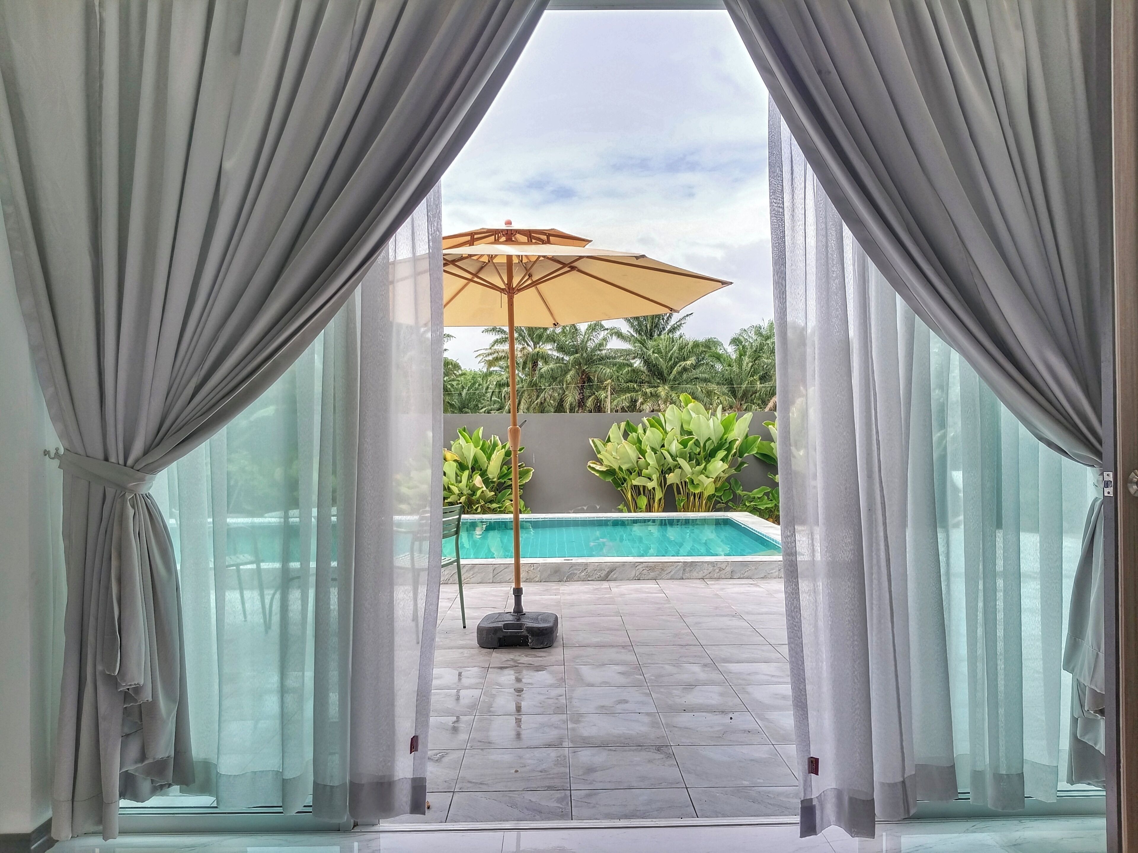 Blick durch eine Tür auf einen Poolbereich mit Deckenventilator und Zimmerpflanzen.