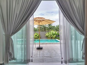 A view through a doorway to a swimming pool area with a ceiling fan and potted plants.