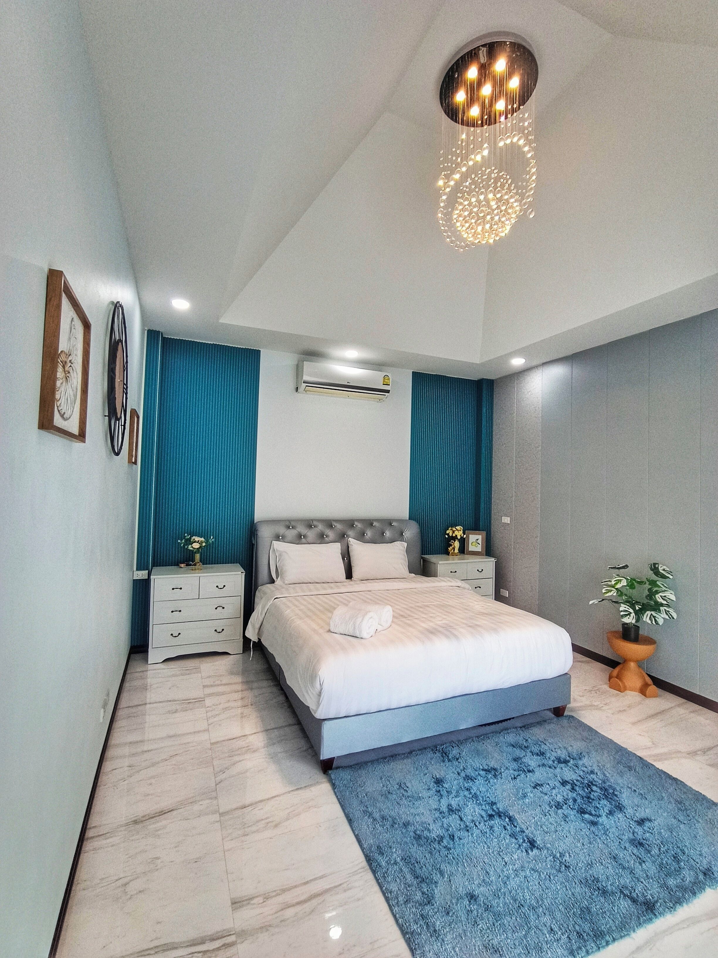 Een moderne slaapkamer met een groot bed, een blauwe accentmuur en een plafondlamp.