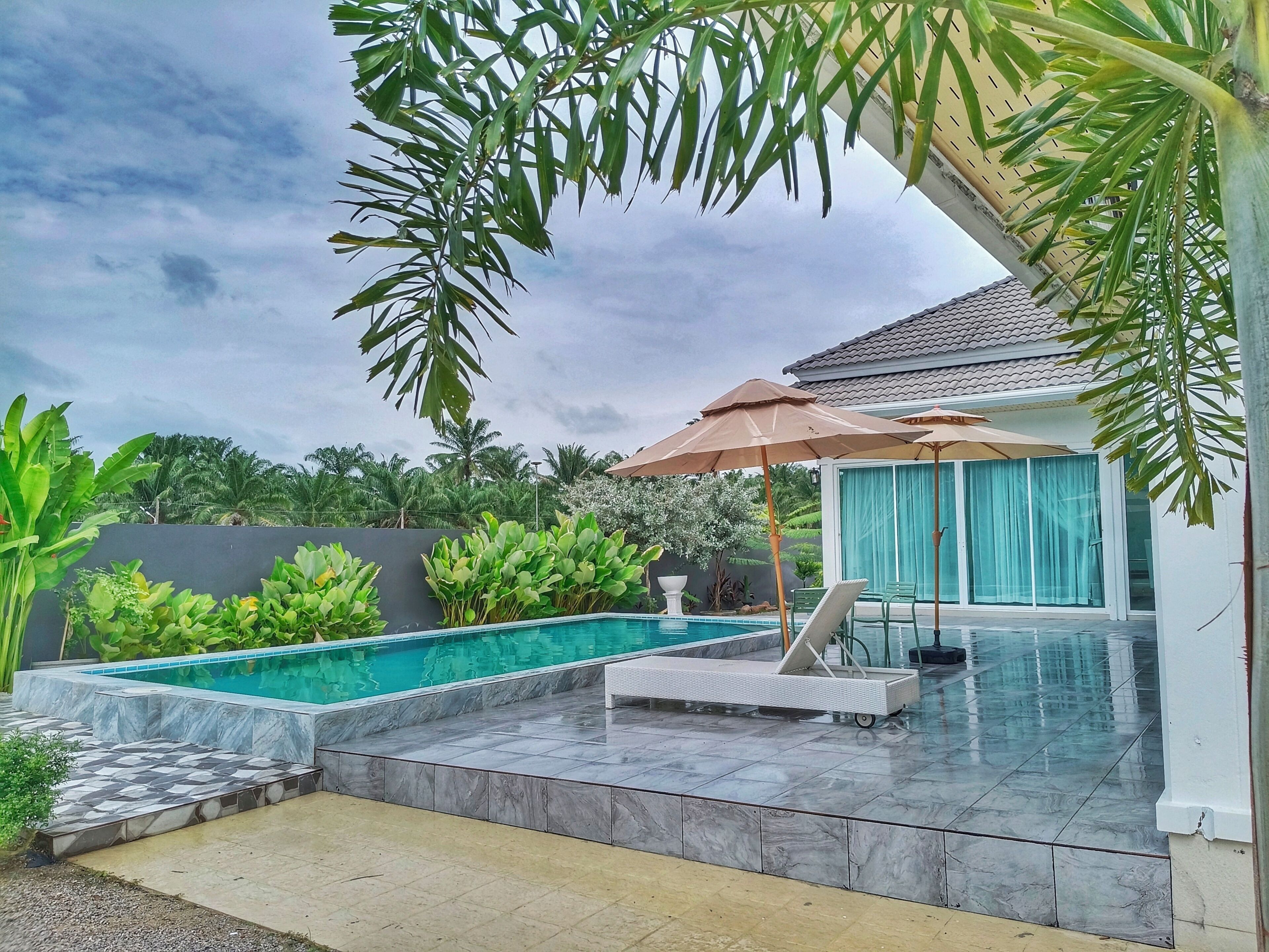 Piscina com deck revestido, espreguiçadeiras e guarda-sóis.