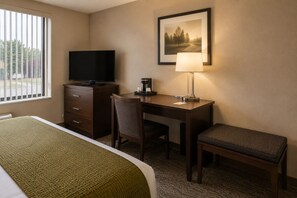 Habitación de hotel con cama, escritorio, silla, televisor, lámpara y un cuadro en la pared.