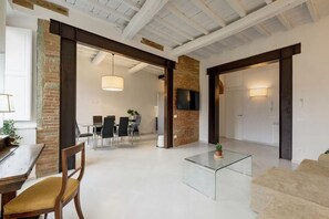 A spacious living area with a glass coffee table, a dining table with chairs, and a kitchen in the background. - Luxury Renovated Apartment with Lift Near Santo Spirito - Sleeps 7 (Firenze)