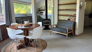 A cozy living room with a round wooden table, white chairs, a grey sofa, and a fireplace.