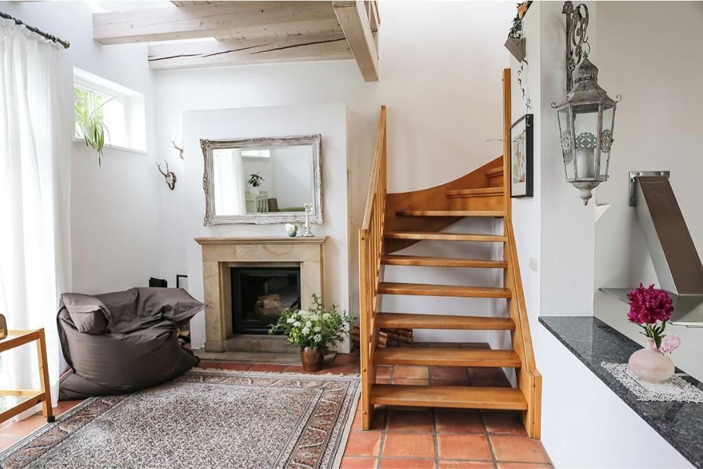 Una habitación con chimenea, una escalera de madera, un sillón informal y un espejo en la pared.
