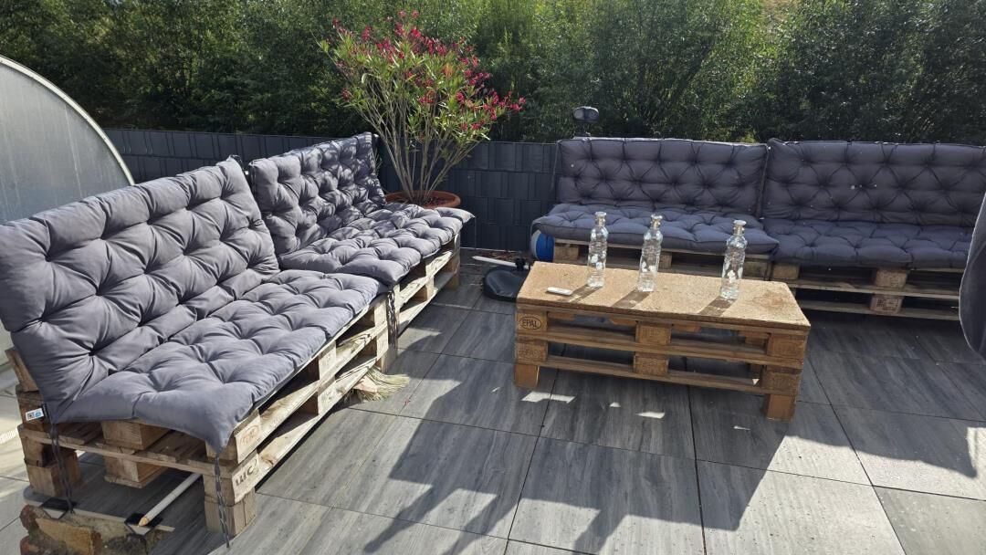 Uma área de estar externa com dois sofás e uma mesa, rodeada por um deck de madeira.