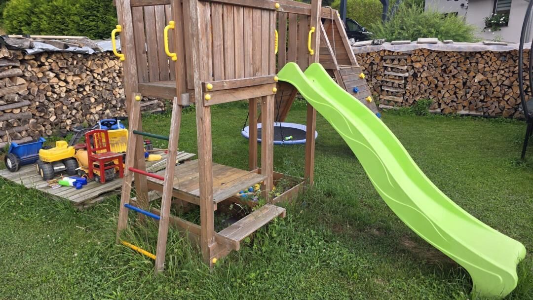 Estructura de juego de madera con un tobogán en un jardín trasero cubierto de césped.