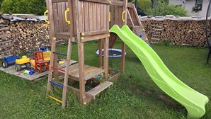 Eine Holzspielanlage mit Rutsche in einem grünen Hinterhof.