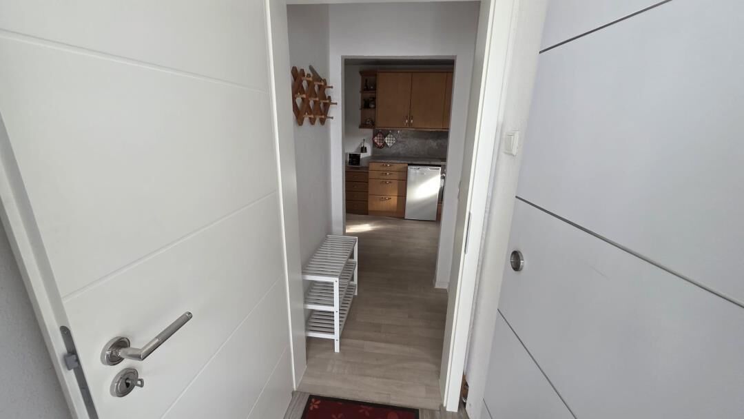 Un pasillo estrecho que conduce a una cocina con armarios de madera y un refrigerador de acero inoxidable.