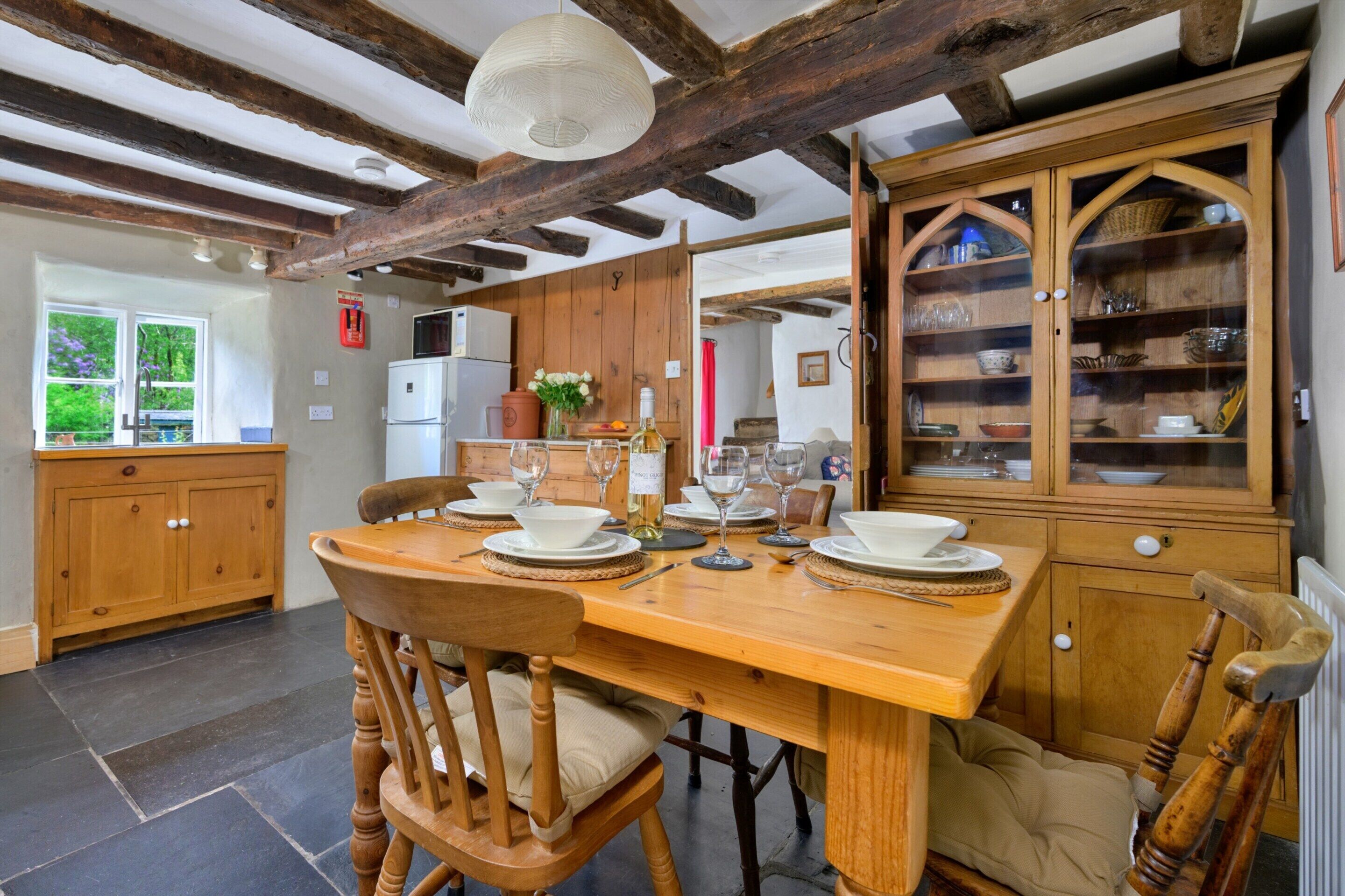 A rustic kitchen with exposed beams, wooden cabinets, and a dining table set for four.