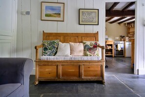 A wooden bench with cushioned seating and decorative pillows, positioned in a room with white paneled walls and a kitchen in the background. - Sea View Lyme Regis House for 9 (Blaenau Ffestiniog)