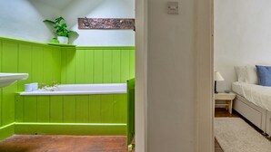 Une salle de bain avec un meuble-lavabo vert, un lavabo blanc et une petite plante en pot.