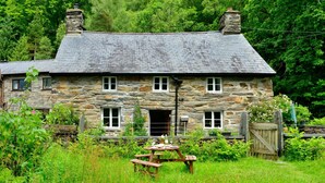 Une petite maison en pierre avec un toit de chaume, une table en bois et un portail.
