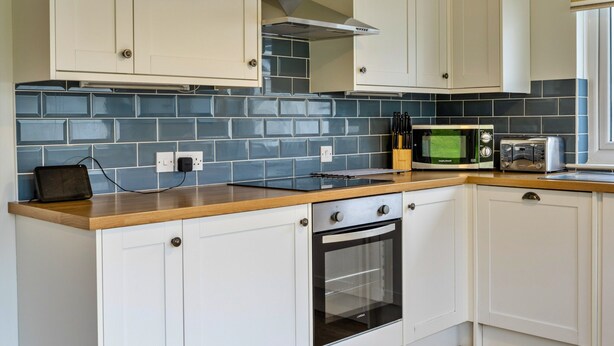 A modern kitchen with white cabinets, a black oven, a microwave, and a toaster. - Kingsand Coastal Retreat for 6 (Bude)