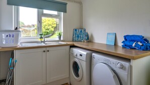 A laundry area with a washing machine, a sink, and a window with a view of greenery. - Kingsand Coastal Retreat for 6 (Bude)
