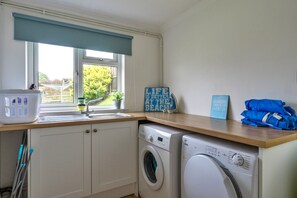 A laundry area with a washing machine, a sink, and a window with a view of greenery. - Kingsand Coastal Retreat for 6 (Bude)