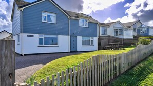A residential building with a blue exterior, a paved driveway, and a wooden fence. - Kingsand Coastal Retreat for 6 (Bude)