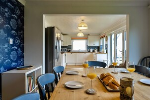 Una cocina moderna con armarios blancos, una mesa de comedor para dos personas dispuesta con platos, vasos y una hogaza de pan.