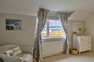Un dormitorio con vistas al mar, un aparador blanco, una silla de mimbre y un radiador.
