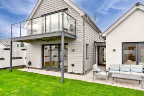 A modern two-story house with a balcony, a patio with outdoor furniture, and a well-maintained lawn. - Coastal Retreat in Westward Ho (Bideford)