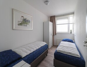 Un dormitorio con dos camas, un armario, un radiador y una ventana con cortinas.