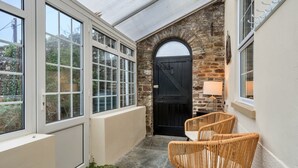 Un rincón acogedor con una puerta negra, ventanas con marco blanco y sillas de mimbre.