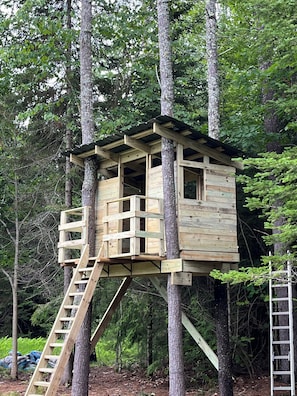 Una casa en un árbol de madera con una escalera, rodeada de bosque.