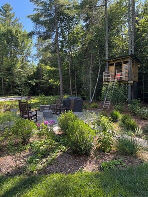 A wooden deck with outdoor furniture, surrounded by lush greenery and a forested area.